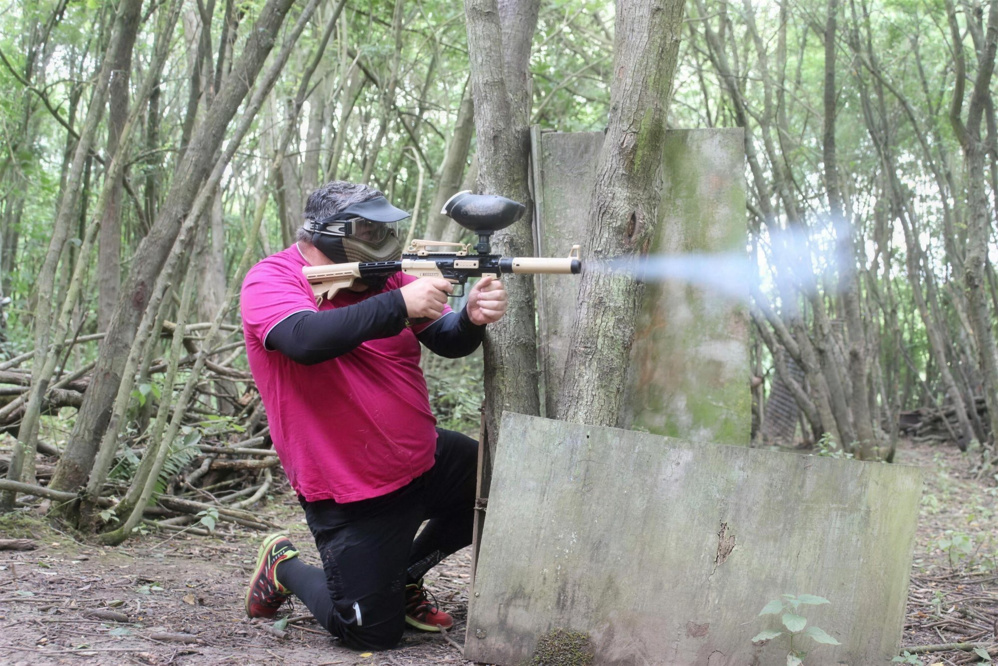 A player in cover firing a paintball marker through the trees at the 1066 site
